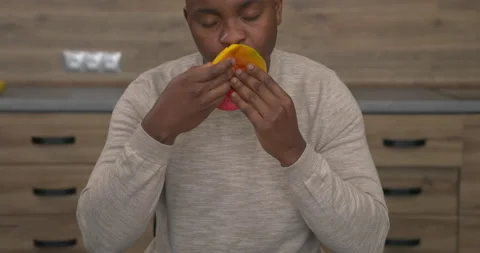 African man sitting at the table and eating fresh sliced mango with appetite. Stock Footage 153281149