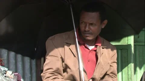 African man sitting under black umbrella protecting from the sun scratching n Vídeo Stock 11410104