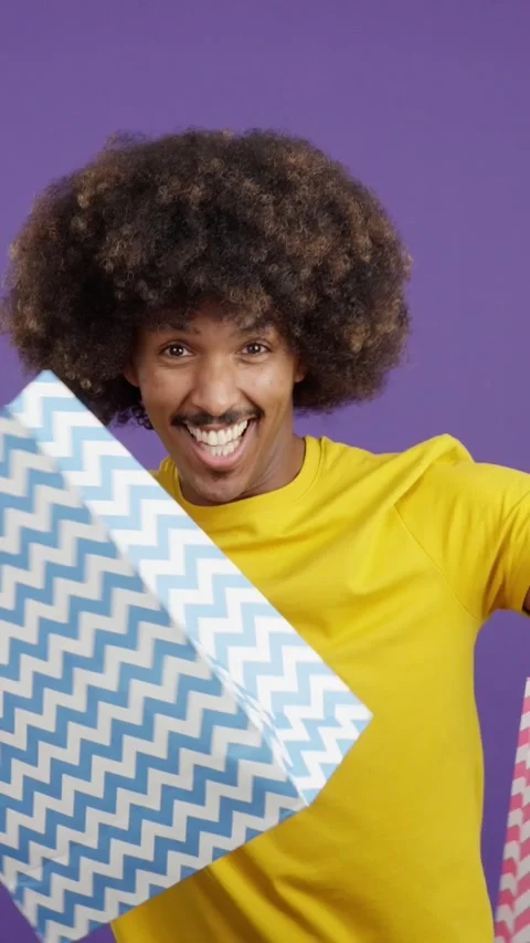 African man smiling at the camera while showing shopping bags Vídeo Stock 244745004