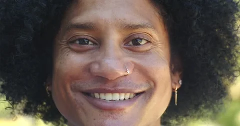 African man smiling into open-mouthed laugh in sunlit park, showing nose hoop Stock Footage 342721673