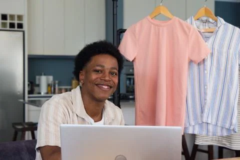 African man smiling while working on laptop at kitchen table with clothing rack Stock Photos