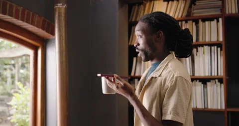 African man standing by arched window in shirt with smartphone, taking call and Stock Footage 336845097