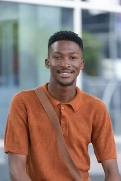 African man standing facing camera by modern glass facade, wearing rust-orange Stock Photos