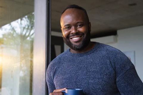 African man standing inside modern home near glass door, in dark-knit sweater Stock Photos