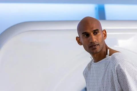 African man standing looking left in imaging room with scanner, hospital gown Stock Photos