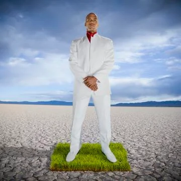African man standing on patch of grass in desert Stock Photos