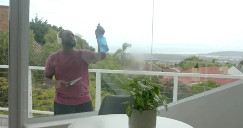African man starting spraying mist and wiping balcony glass with squeegee, Video stock 338436202