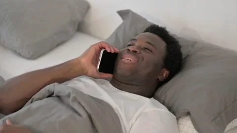 African Man Talking on phone while Lying in Bed Stock Footage 299756624