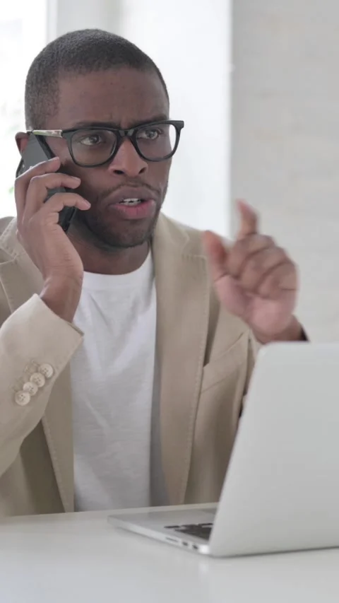 African Man Talking on Smartphone while using Laptop in Office, Vertical Video Stock Footage 337350092