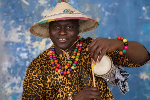African man in traditional clothes and fulani hat playing on talking drum Stock Photos
