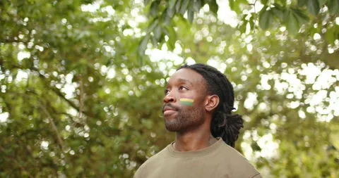 African man under leaves sun drawing gaze up responding to camera by turning and Stock Footage 340457328