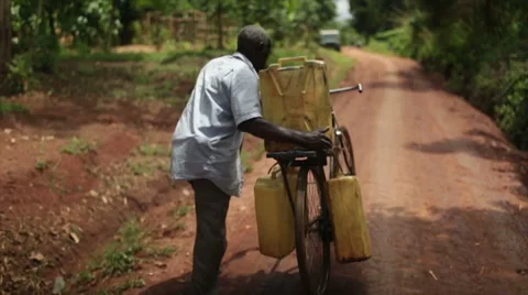 African man using a bicycle to collect water in 3 containers pushing bike Stock Footage 54999715