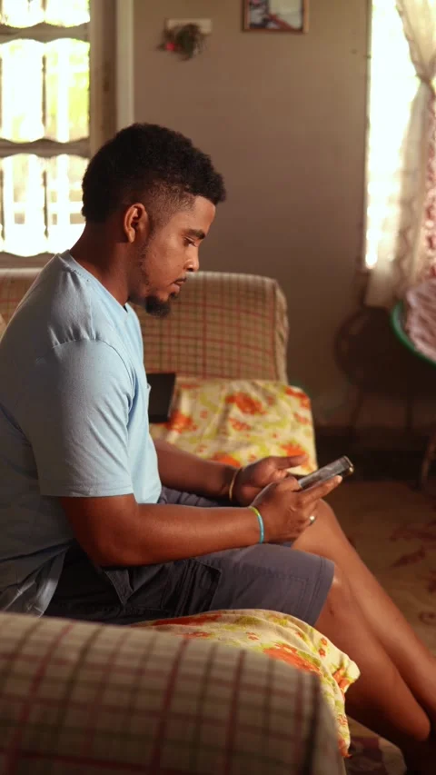 African man using a smartphone at home on the sofa Video stock 328178016