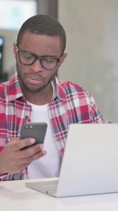 African Man using Smartphone while using Laptop, Vertical Video Stock Footage 340040218