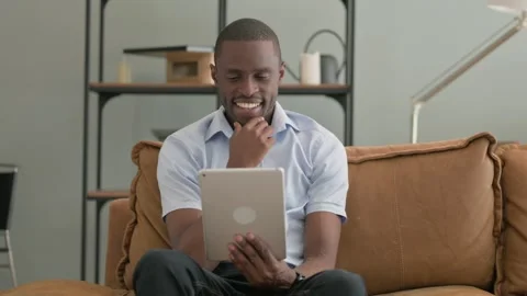 African Man Using Tablet while Sitting on Sofa at Home Stock Footage 287914486
