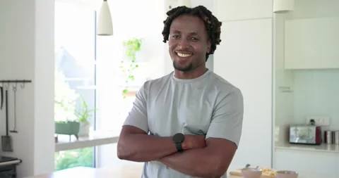 African man wearing gray tee, watch at kitchen island as camera zooming, smiling Stock Footage 334924542