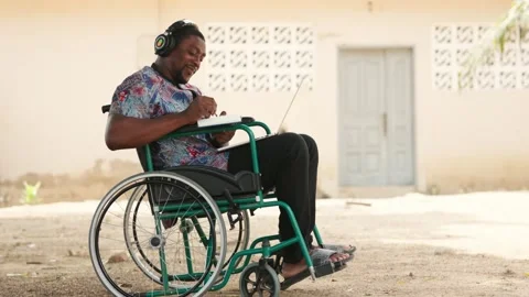 African Man in Wheelchair Using Laptop Outdoors for Remote Work &amp; Online Access 動画素材 346244480