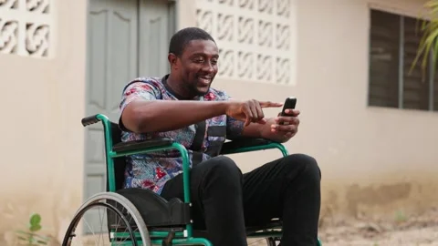 African Man in Wheelchair Using Mobile Phone for MoMo Outdoors: Inclusion Stock Footage 346244893