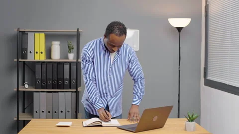 African man working on laptop looking at camera smiling standing at office Stock Footage 264512137
