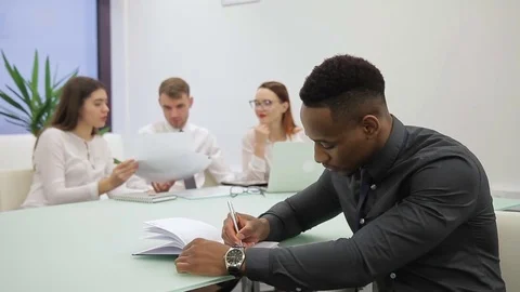 African man writes in notebook while sitting at table in modern office. Video stock 85404901
