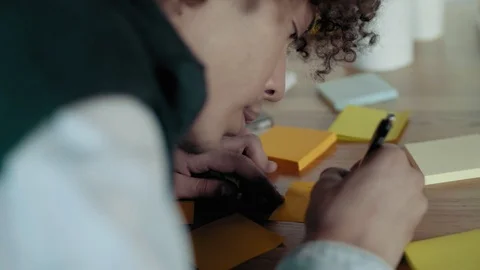 African man writes reminders notes on sticky multicolored stickers leaning over Video stock 93790472