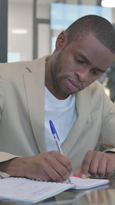 African Man Writing Documents at Work, vertical video Stock Footage 324791785