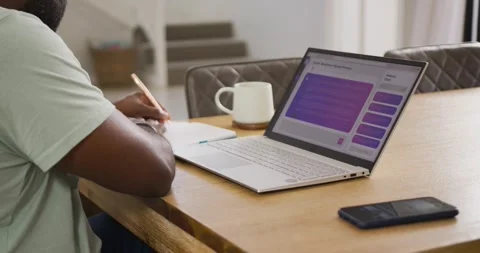 African man writing in notebook using purple laptop prompts and pencil at wooden Stock Footage 335071852