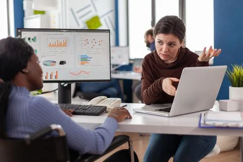 African manager with mask working checking graphs, coworker holding laptop Foto stock