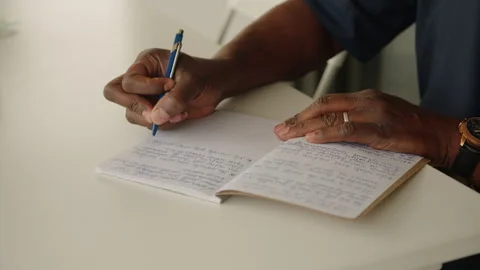 African man's hand writing on a notebook on a white table, medium shot Stock Footage 336529707