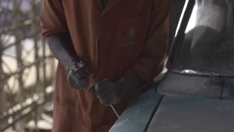 African mechanic, hammers chisel to remove paint from vehicle, slo-mo. Stock Footage 82329441