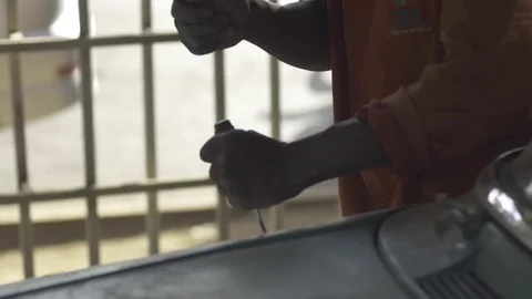 African mechanic, hammers chisel to remove paint from vehicle, slo-mo. Stock Footage 82329446