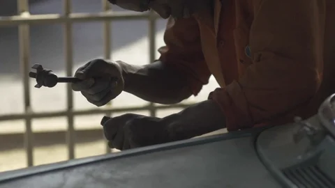 African mechanic, hammers chisel to remove paint from vehicle, slo-mo. Stock Footage 82329459