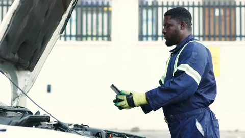 African mechanic uses tablet to inspect car engine in workshop Stock Footage 346641489