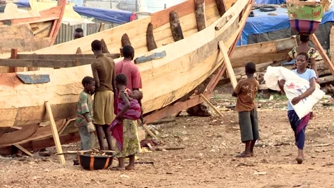 African men are building a large wooden boat. A boy and a girl help them. A Stock Footage 155570039