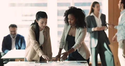 African mentor explaining project details to young Asian colleague apprentice Stock Footage 268624301