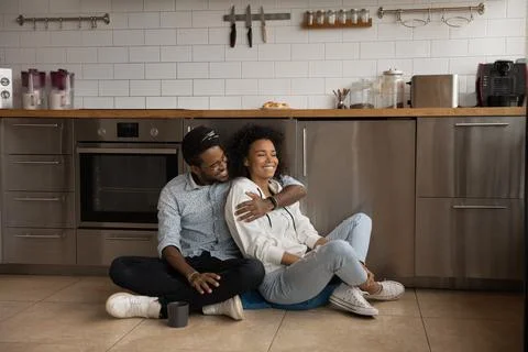 African millennial couple sit on floor in the kitchen Stock Photos