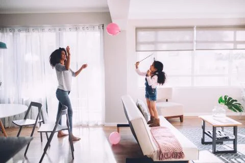 African mother and daughter playing with balloon in living room Stock Photos