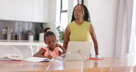 African mother replying to homework leaning over child writing at dining table Stock Footage 340011167