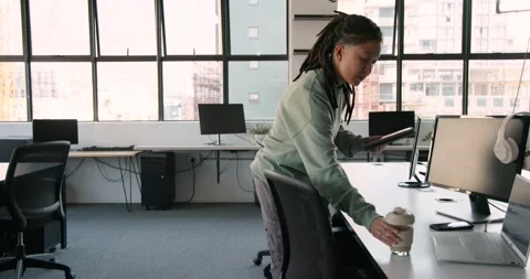 African non-binary person entering office reading tablet sipping cup typing on Stock Footage 342033190