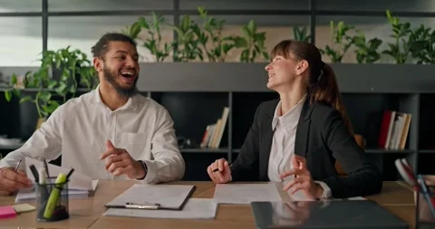 African office worker laughs and chats with a colleague at the table enjoying a Stock Footage 307489359