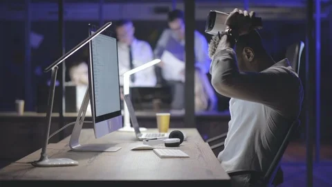 African office worker using VR goggles and computer in dark office. Stock Footage 125691075