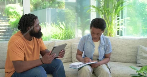 African parent using tablet leading lesson while teenage student writing Stock Footage 337097648