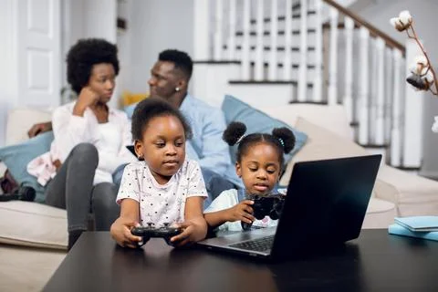 African parents resting on sofa while kids playing on laptop 스톡 사진