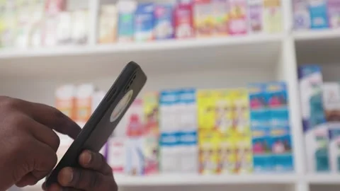 African Pharmacist Using Smartphone to check available Medicines in Drugstore Stock Footage 345512041