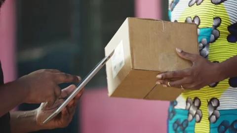 African Postal Delivery Man records receipt details of shipped box parcel. Stock Footage 345522981