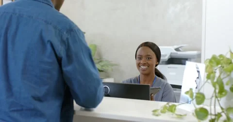 African receptionist smiling, entering check-in on computer as male visitor Stock Footage 344948667