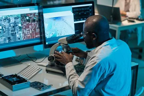 African scientist with microscope working in front of computer monitors Foto stock