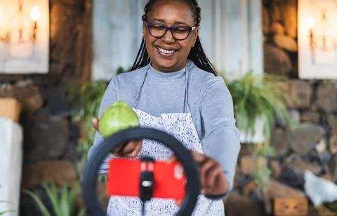 African senior woman preparing food recipe while streaming with mobile phone Stock Photos