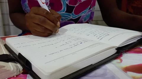 African sitting, writing slowly with white pen in diary. Stock Footage 315544737