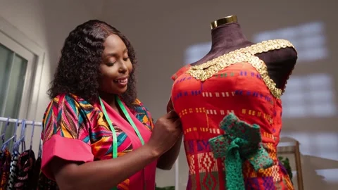 African tailor meticulously working on traditional print dress on mannequin  Stock Footage 346788571